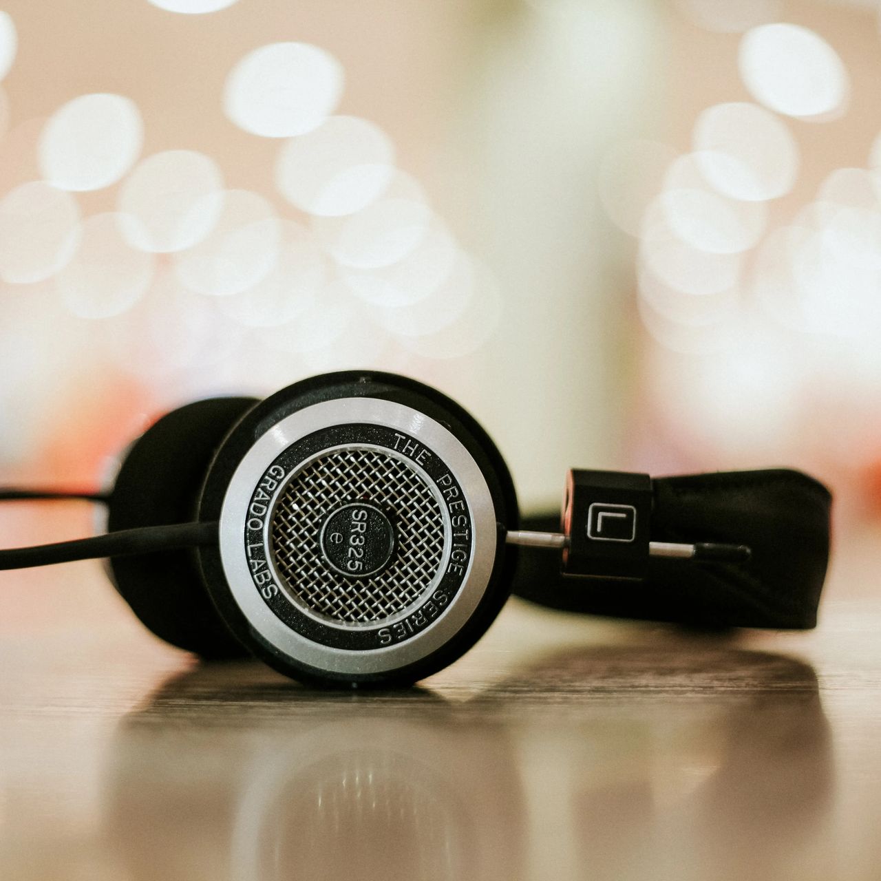 Close-up of a pair of black headphones resting on a surface, with a blurred, colorful bokeh background.