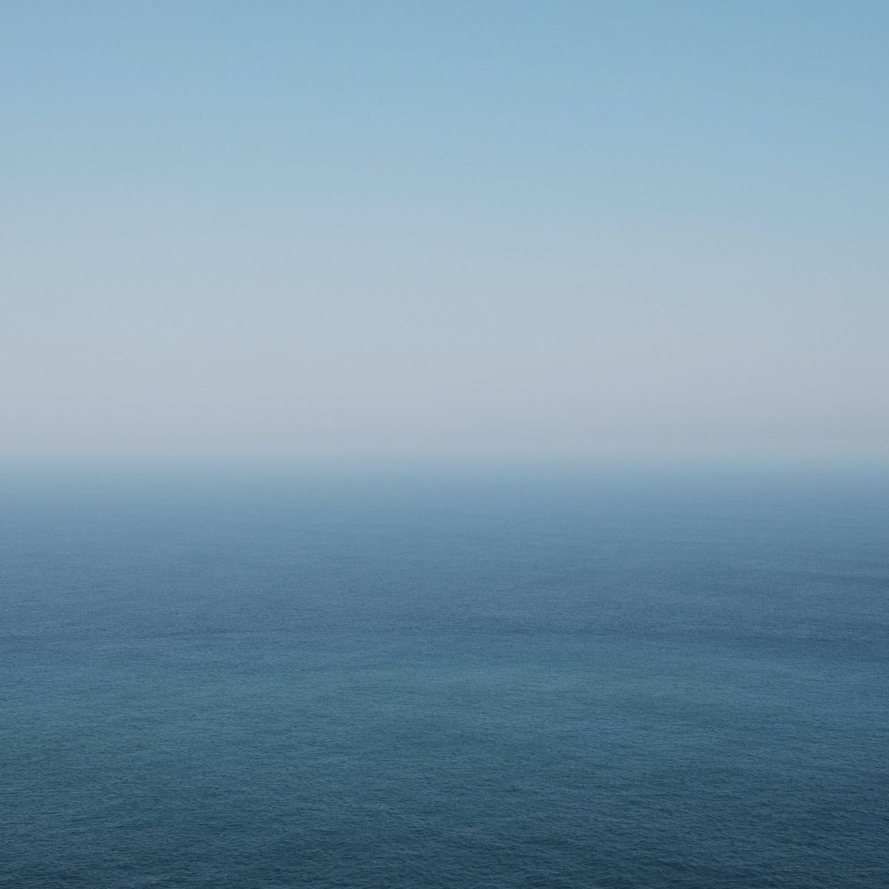 A serene seascape featuring a gradient of blue hues, transitioning from light to deep blue, under a clear sky. The horizon blends seamlessly with the water, creating a tranquil, minimalist effect.