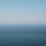 A serene seascape featuring a gradient of blue hues, transitioning from light to deep blue, under a clear sky. The horizon blends seamlessly with the water, creating a tranquil, minimalist effect.