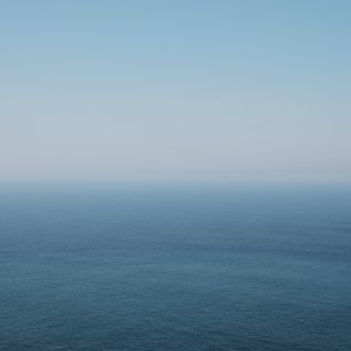 A serene seascape featuring a gradient of blue hues, transitioning from light to deep blue, under a clear sky. The horizon blends seamlessly with the water, creating a tranquil, minimalist effect.