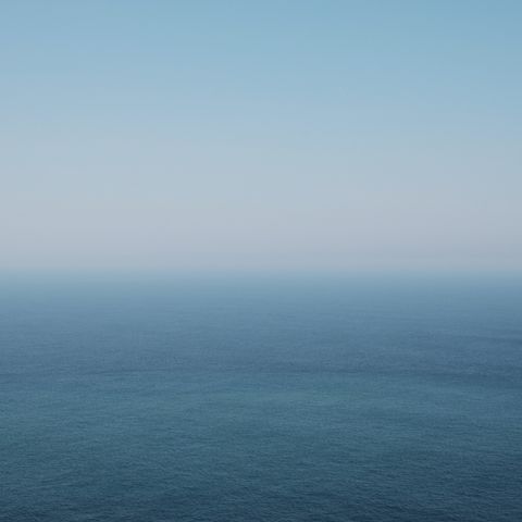 A serene seascape featuring a gradient of blue hues, transitioning from light to deep blue, under a clear sky. The horizon blends seamlessly with the water, creating a tranquil, minimalist effect.