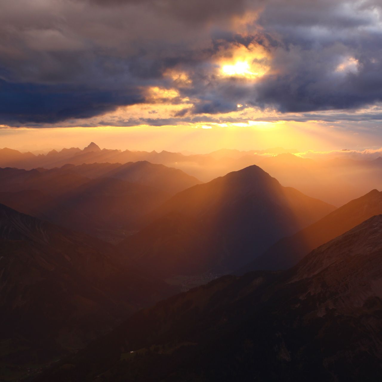 An album cover featuring a dramatic sunset over layered mountain ranges, with beams of light breaking through clouds and illuminating the landscape in warm golden hues.