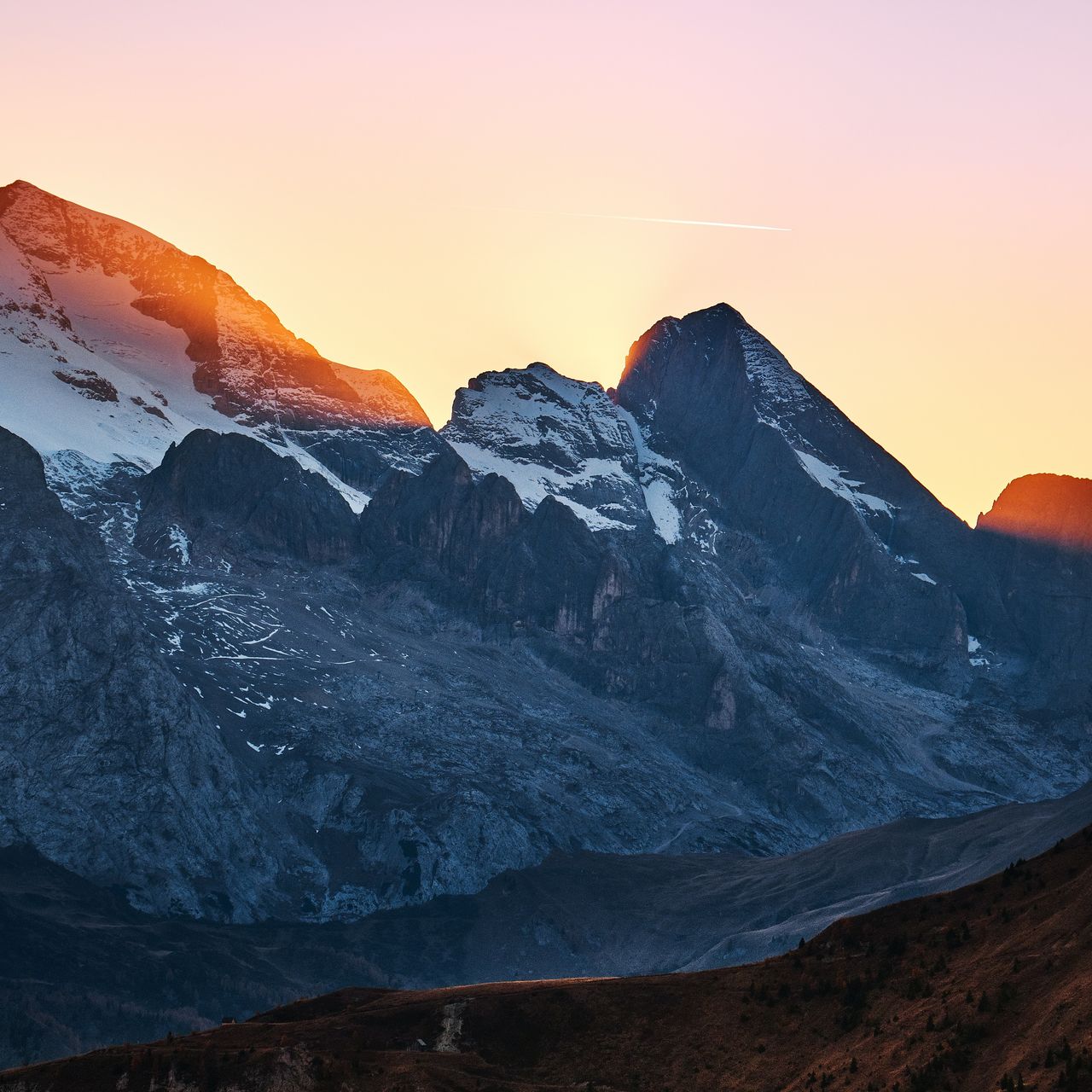 A majestic mountain landscape at sunset, featuring snow-capped peaks and a gradient sky transitioning from orange to pink.