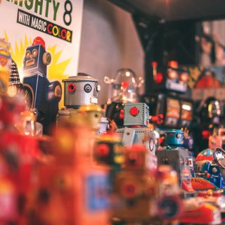 A collection of vintage toy robots, some colorful and metallic, arranged on a shelf with a retro-style album cover in the background that reads "Mighty 8 with Magic Color."